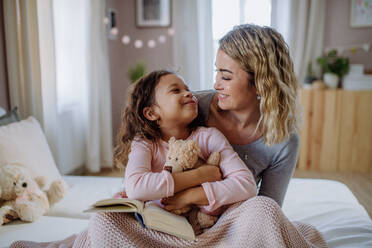 Eine glückliche Mutter, die ihre kleine Tochter im Arm hält und sich im Bett ansieht. - HPIF02897