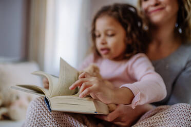 Eine glückliche Mutter mit ihrer kleinen Tochter, die zu Hause auf dem Bett sitzt und ein Buch liest. - HPIF02898