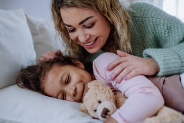 A happy mother stroking her little daughter when lying on bed with her at home. - HPIF02902