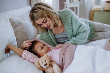 Eine glückliche Mutter, die ihre kleine Tochter streichelt, während sie mit ihr zu Hause im Bett liegt. - HPIF02903