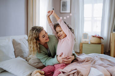 Eine glückliche Mutter streichelt ihre kleine Tochter, die sich morgens beim Aufwachen im Bett streckt. - HPIF02904