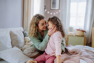 Eine glückliche Mutter, die ihre kleine Tochter streichelt und die gemeinsame Zeit im Bett zu Hause genießt. - HPIF02905