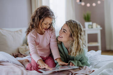 A happy mother with her little daughter sitting on bed and using tablet at home. - HPIF02917