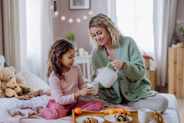 A happy mother with her little daughter having breakfast together in bed at home. - HPIF02920