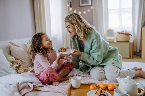 Eine glückliche Mutter mit ihrer kleinen Tochter beim gemeinsamen Frühstück im Bett. - HPIF02923