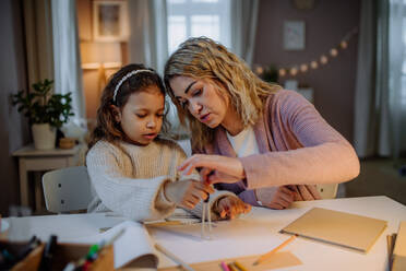 A mother helping her daughter with homework, drawing a circle with comasses in evening at home. - HPIF02924