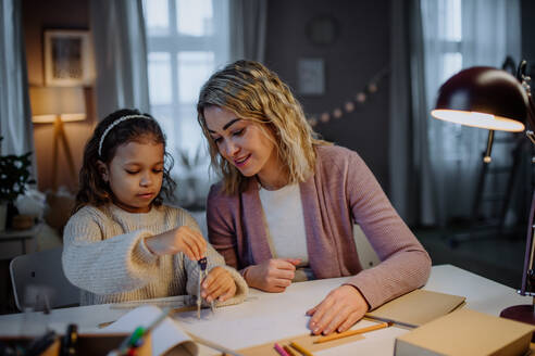 Eine Mutter hilft ihrer Tochter bei den Hausaufgaben, indem sie am Abend zu Hause einen Kreis mit Zirkeln zeichnet. - HPIF02925