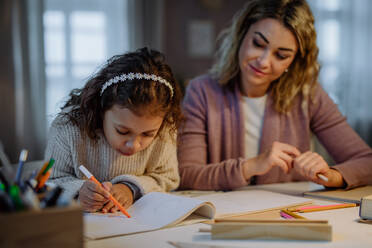 A little girl doing homework with her mother in evening at home. - HPIF02926
