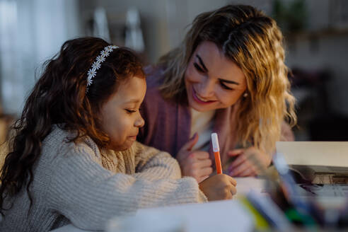 Ein kleines Mädchen macht abends zu Hause mit seiner Mutter Hausaufgaben. - HPIF02929
