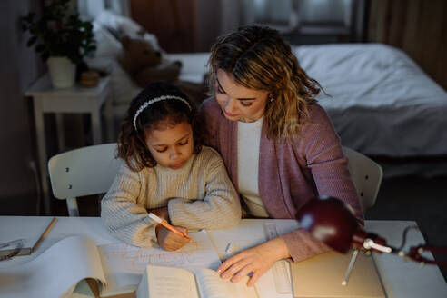 Eine hohe Winkel Ansicht des kleinen Mädchens tun Hausaufgaben mit ihrer Mutter am Abend zu Hause. - HPIF02933