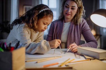 Eine Mutter hilft ihrer Tochter bei den Hausaufgaben, indem sie am Abend zu Hause einen Kreis mit Zirkeln zeichnet. - HPIF02936