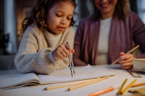 Eine Mutter hilft ihrer Tochter bei den Hausaufgaben, indem sie am Abend zu Hause einen Kreis mit Zirkeln zeichnet. - HPIF02937