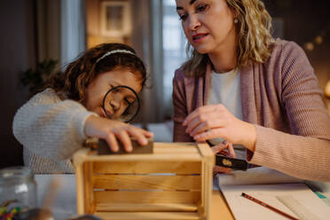 A happy little girl renovating a wooden crate together with her mother at home. - HPIF02943