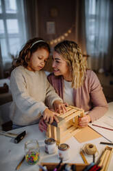 Ein fröhliches kleines Mädchen, das zusammen mit seiner Mutter zu Hause eine Holzkiste renoviert. - HPIF02948