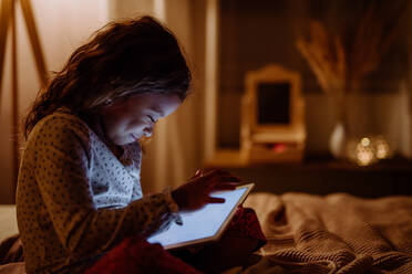 A happy little multiracial girl using tablet on bed in evening at home. - HPIF02955
