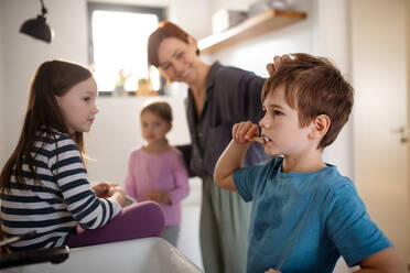 Eine Mutter mit drei kleinen Kindern im Badezimmer beim Zähneputzen. - HPIF02965