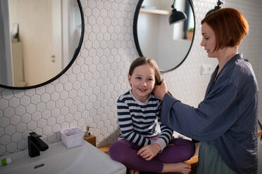 Eine Mutter bürstet ihrer kleinen Tochter im Badezimmer die Haare, Morgenroutine Konzept. - HPIF02975