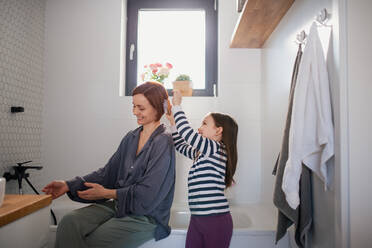 Ein kleines Mädchen bürstet ihrer Mutter im Badezimmer die Haare, Konzept der täglichen Routine. - HPIF02977