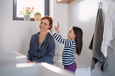 Ein kleines Mädchen bürstet ihrer Mutter die Haare im Badezimmer, Morgenroutine Konzept. - HPIF02978