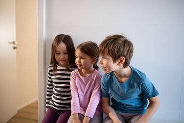 Die drei kleinen Geschwisterkinder sitzen zu Hause. - HPIF02979