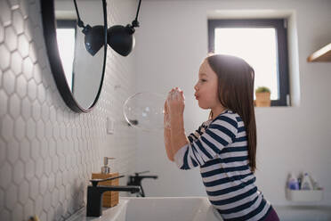 Ein kleines Mädchen im Badezimmer, das sich die Hände wäscht und Seifenblasen macht. - HPIF02993