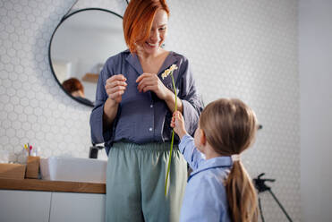 A little girl congratulates mother and gives her flower in bathroom at home. - HPIF02997