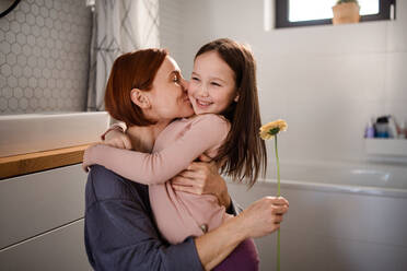 A little girl congratulates mother and gives her flower in bathroom at home. - HPIF03004