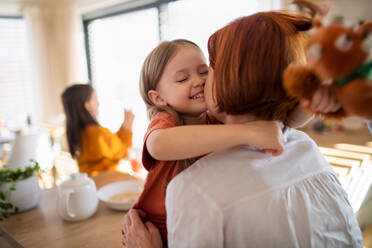Eine Rückansicht einer Mutter, die ihre kleine Tochter in der Küche zu Hause umarmt. - HPIF03026