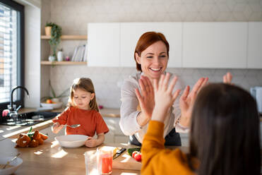 Eine glückliche Mutter, die sich mit ihrer kleinen Tochter beim Frühstück in der Küche zu Hause die Hände reibt. - HPIF03028