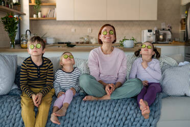 Drei kleine Kinder mit einer Mutter, die zu Hause auf dem Sofa sitzen und sich Gurken ins Gesicht schmieren. - HPIF03054