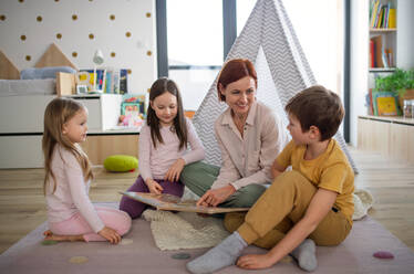 Eine fröhliche Mutter von drei kleinen Kindern, die ihnen zu Hause ein Buch vorliest. - HPIF03071