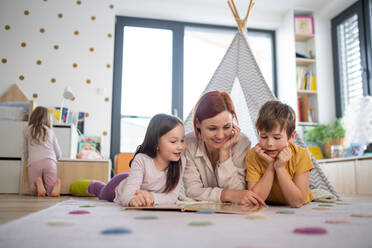 Eine fröhliche Mutter von drei kleinen Kindern, die ihnen zu Hause ein Buch vorliest. - HPIF03072