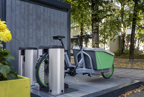 Germany, Bavaria, Munich, Electric rental cargo bike charging at station - MAMF02330