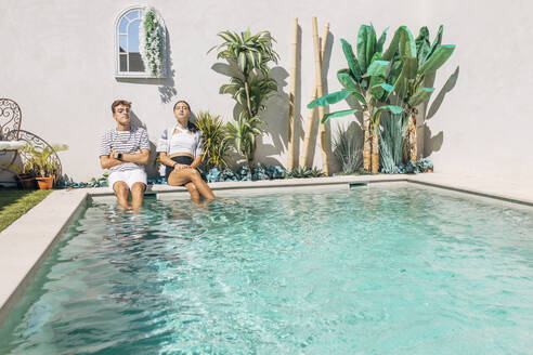 Brother and sister relaxing by swimming pool on sunny day - EGHF00676