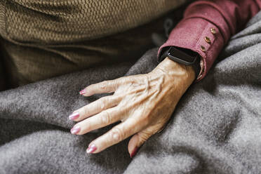 Hand einer älteren Frau mit intelligenter Uhr über einer Decke - LJF02327