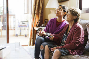 Happy senior woman watching TV with caregiver at home - LJF02338