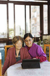 Lächelnde Krankenschwester bringt einer älteren Frau zu Hause einen Tablet-PC bei - LJF02345