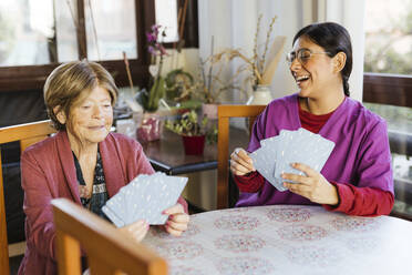 Glückliche Mitarbeiterin im Gesundheitswesen spielt Karten mit einer älteren Frau zu Hause - LJF02347
