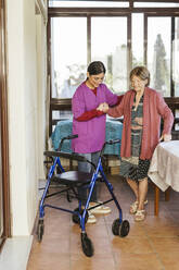 Young caregiver helping senior woman to walk at home - LJF02349