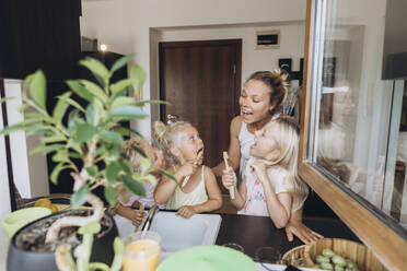 Mutter beobachtet Töchter beim Zähneputzen mit Holzbürsten in der Küche - SIF00561