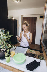 Glückliche Frau schaut in der Küche auf ihr Mobiltelefon - SIF00584