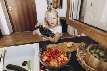 Girl preparing a salad in the kitchen pouring oil into bowl - SIF00597