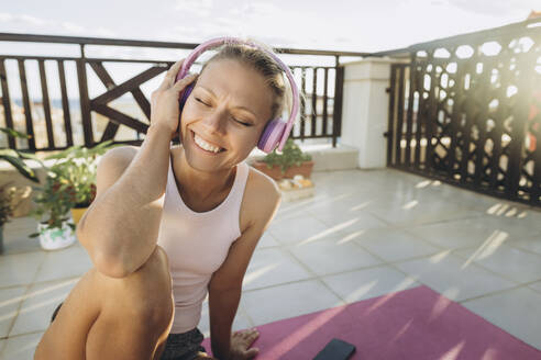 Glückliche Frau, die auf der Terrasse mit Kopfhörern Musik hört - SIF00625