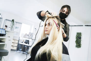 Young hairdresser curling customer's hair in salon - NJAF00063