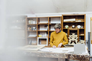 Mature craftsman sketching standing at workbench in workshop - MEUF08797