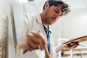 Craftsman wearing lab coat working in workshop - MEUF08832