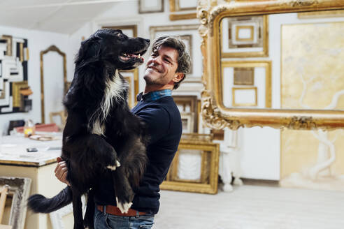 Lächelnder reifer Mann mit Hund in einer Werkstatt - MEUF08839