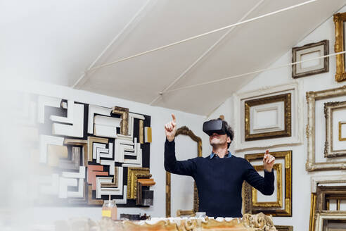 Älterer Mann benutzt einen Virtual-Reality-Simulator und gestikuliert in einer Werkstatt - MEUF08843
