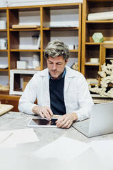 Craftsman wearing lab coat using tablet PC in workshop - MEUF08845