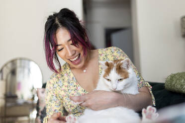 Happy young woman playing with cat at home - WPEF06833